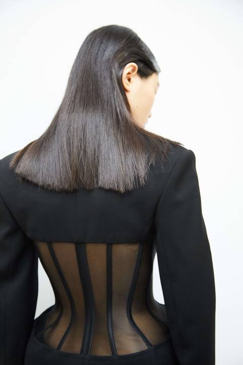 Model from the back in Mugler black and mesh corset jacket with straight black hair and side profile of face
