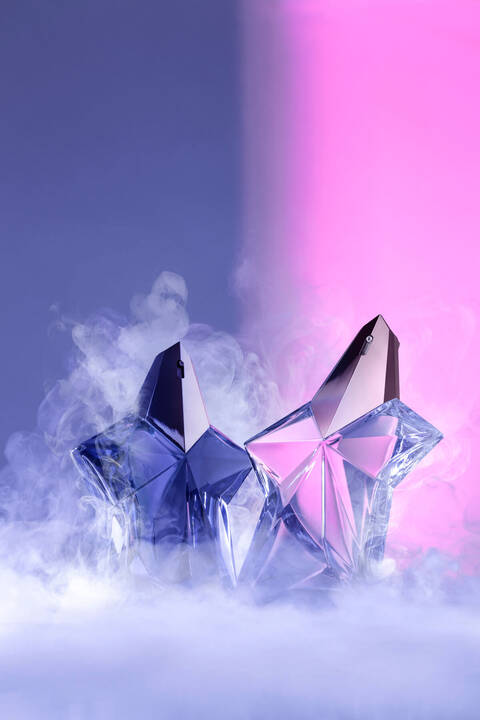Two Mugler Angel fragrance bottles on neon purple and pink background in smoke
