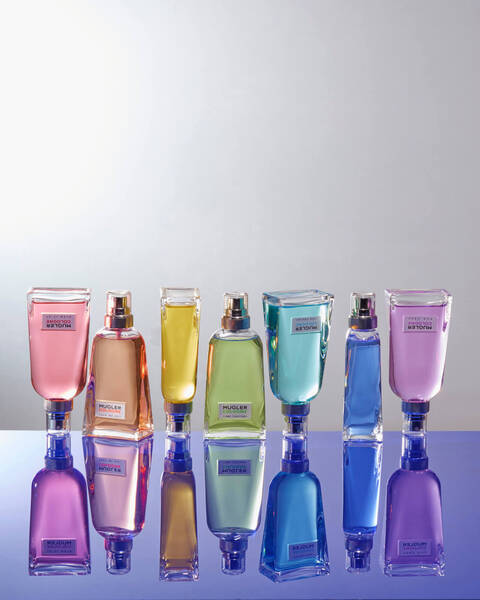 Seven Mugler Cologne bottles in rainbow order both right side up and upside down with glass reflection