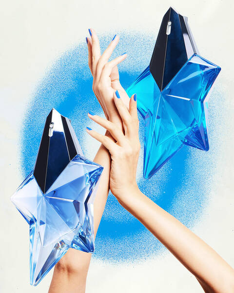 Pair of hands with blue nail polish to match blue Mugler Angel bottles and blue ring background