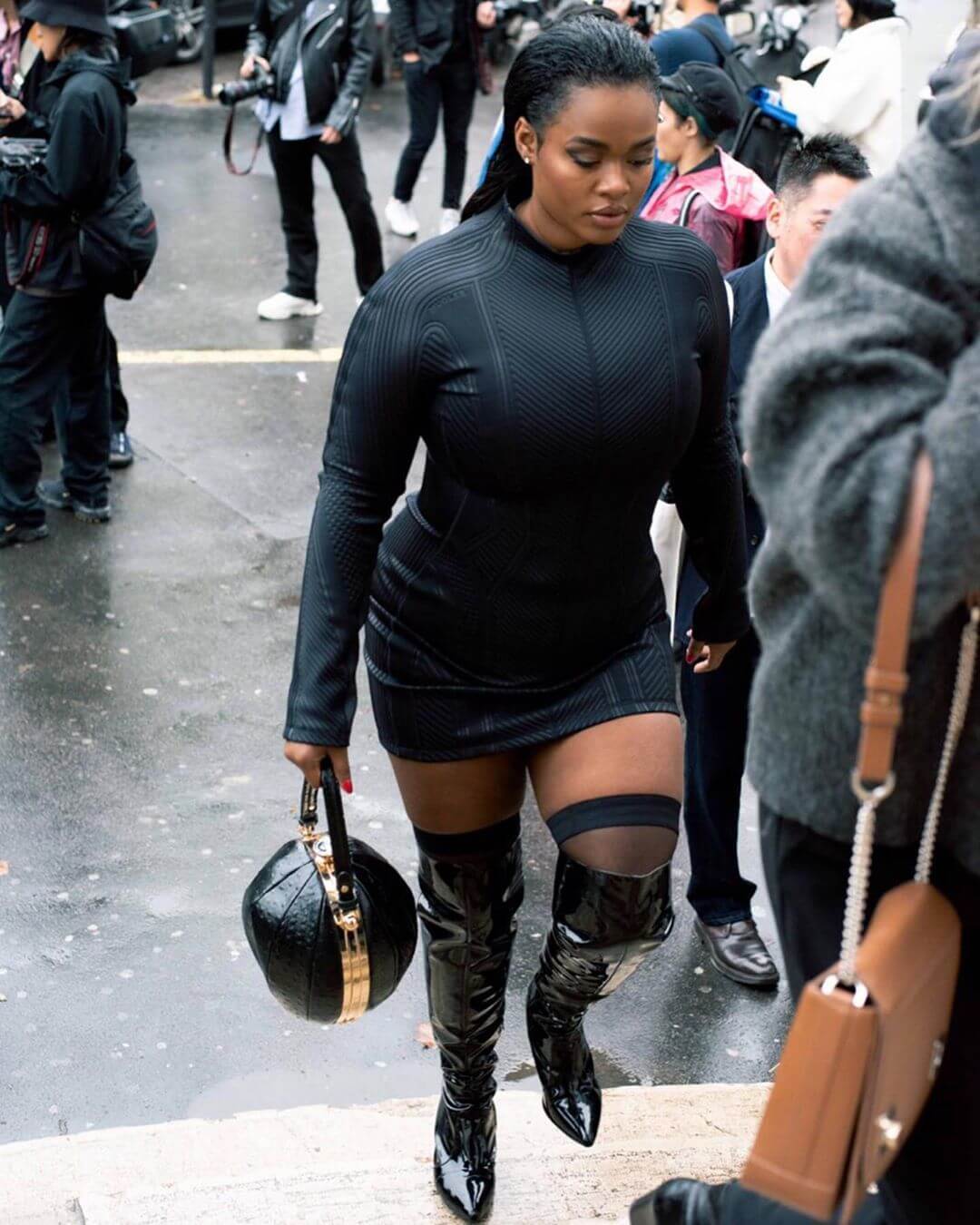 Woman walking up stairs wearing tight black body dress and high black boots for Mugler