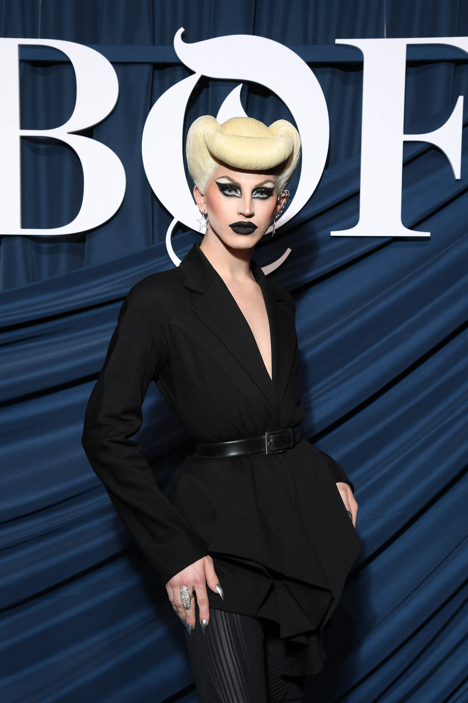 Woman with large blonde bun, heavy makeup and black pantsuit for Mugler Magazine